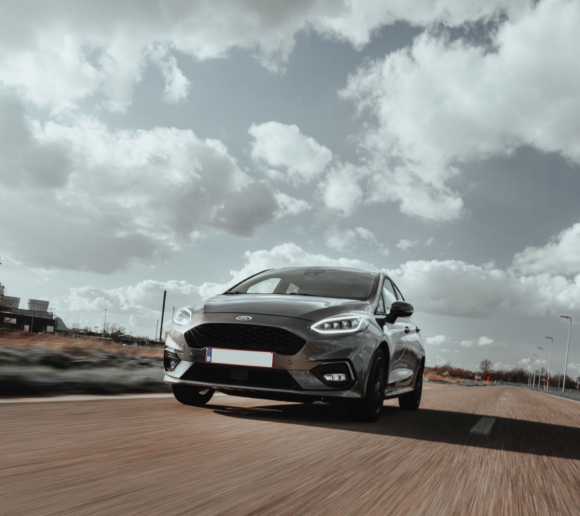 A hatchback in motion on an open road under a dramatic sky